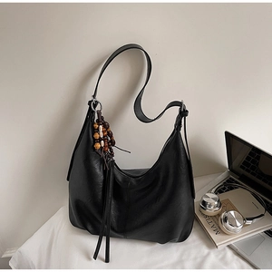 Detail of a matte black hobo bag featuring a wooden bead and leather tassel charm accessory
