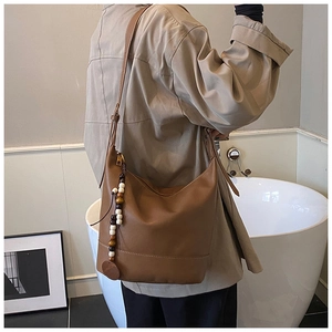 Detail view of brown leather hobo bag with white stitching and wood bead charm