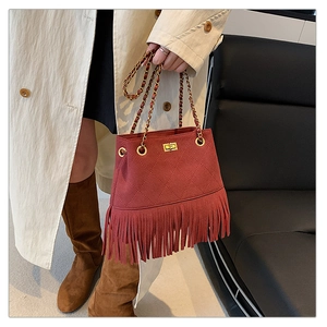 Detail of red quilted chain bucket bag with long tassels held by a model in a trench coat