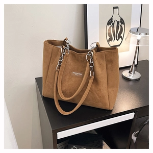 Detail of a brown suede tote bag with chain strap and metallic brand logo plate