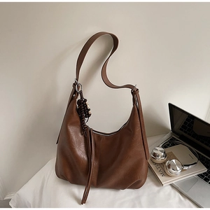 Detail of dark brown faux leather hobo bag with tassel and wooden bead charms on white bed