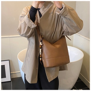 Detailed view of brown leather crossbody bag featuring a unique wooden bead pendant accessory