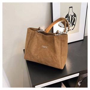 Detailed view of the brown faux suede tote bag with chain link handles and leather patch