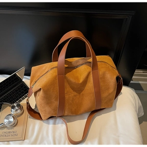 Brown suede tote bag with leather straps on bed next to a laptop and headphones