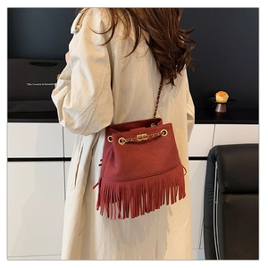 Detail of brick red bucket bag with fringe trim, quilted pattern and gold chain strap