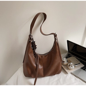 Brown leather hobo bag with unique wood bead charm and tassels on a cozy bed setup