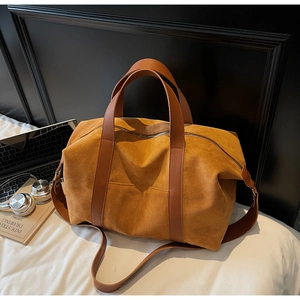 Close-up of brown suede travel tote bag with double handles and adjustable strap on bed