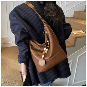 Detail of soft brown leather tote bag with decorative bead charm on a blue blazer model