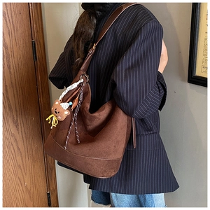 Détail d'un grand sac cabas en daim marron avec pendentif ours sur blazer à rayures