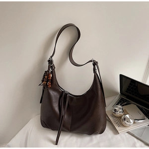 Detail of dark brown leather half-moon shoulder bag with wooden bead charm and zipper