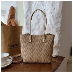 Détail de la texture tressée beige et des fermoirs métalliques argentés du sac cabas