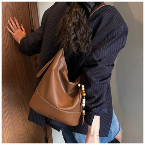 Detail of brown leather tote bag with white stitching and boho beaded tassel charm