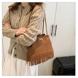 Detail of brown suede bucket bag featuring fringe trim, quilted pattern and gold chain strap
