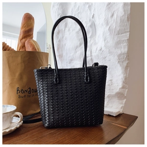 Détail du sac seau tressé noir avec doubles poignées et bandoulière amovible