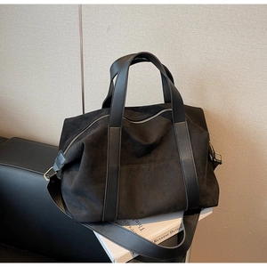 Detail view of large black matte tote bag with contrast leather handles and bronze hardware