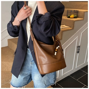 Detail of dark brown leather hobo bag featuring beaded strap charm and wide shoulder strap