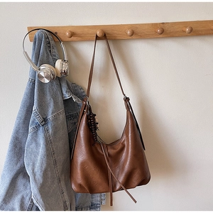 Detail of vintage brown leather hobo bag with tassel hanging on a wooden hook