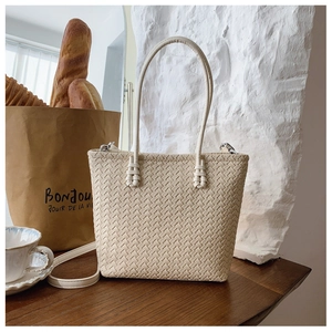 Détail de la texture du sac cabas tressé crème avec bandoulière sur table rustique