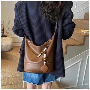 Detail of brown leather tote with wooden bead charm and white contrast stitching on base