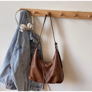 Brown vintage large hobo bag with fringe details hanging on a wooden coat rack