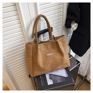 Detail of a brown suede tote bag with brand label and silver metal ring handle