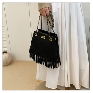 Close-up of black suede tassel bucket bag with gold lock and chain strap on white dress