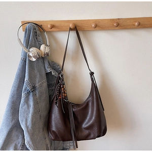 Detail of dark brown leather hobo bag with wood bead charm hanging on a rack