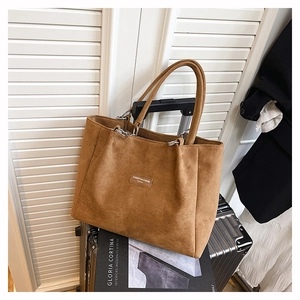 Detail of a brown suede tote bag featuring silver hardware on a metallic suitcase
