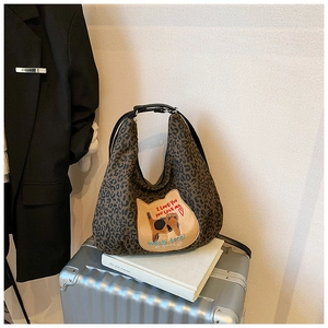 Détail du sac hobo léopard avec écusson chat sur une valise en argent métallique