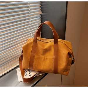Close-up of yellow suede tote bag with brown leather straps by a window with blinds