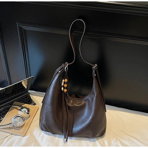 Detail of a large brown shoulder bag with a wooden bead tassel on a commuter desk
