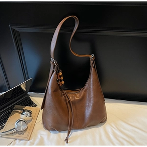 Detail of brown hobo bag with tassel and wood bead charm on a white bedsheet