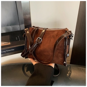 Detail of dark brown suede crossbody bag showing quilted pattern and patent leather trim