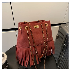 Detail of burgundy suede bucket bag featuring diamond quilting and long tassel trim