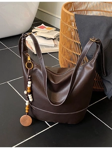 Large brown tote bag with contrast stitching and beaded tassel on dark floor background