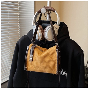 Detail view of yellow quilted crossbody bag with brown leather trim on black hoodie
