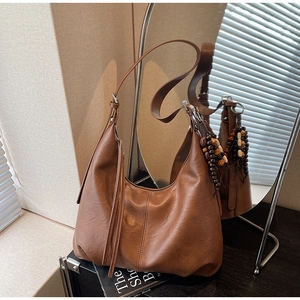 Detail view of brown leather hobo bag with fringe tassels and wooden bead charm accessory