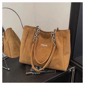Detail of dark brown suede tote bag featuring a leather logo tag and silver chain handle