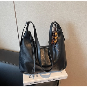 Detail of black leather shoulder bag with zipper and decorative wooden bead pendant