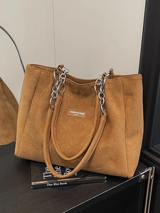 Brown suede tote bag with stylish silver chain strap and minimalist logo on white background