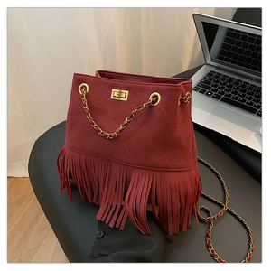 Detail of burgundy suede bucket bag with long tassels and quilted pattern on a gray stool