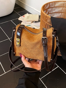 Brown suede crossbody bag with quilted stitching and vintage clasp detail shown by hand