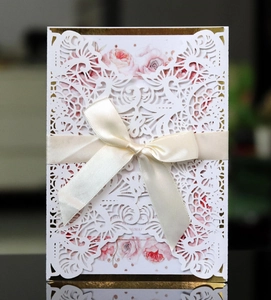Detail of laser cut wedding invitation with floral insert and cream satin ribbon bow