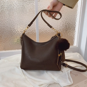 Deep brown faux leather shoulder bag with plush ball and tassel charm on a model