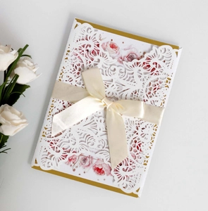 Detailed laser cut lace wedding invitation with gold backing and cream silk ribbon bow