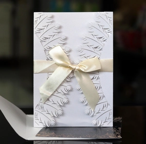 Detailed laser-cut white feather pattern invitation card with champagne silk bow