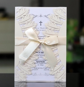 Detail of ivory laser-cut wedding invitation with satin bow and intricate feather pattern
