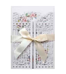 Laser cut white wedding invitation card with elegant floral patterns and beige ribbon bow