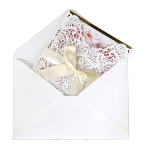Detail of laser-cut wedding invitation with pink floral insert and cream silk ribbon