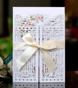 Detailed laser-cut white wedding invitation with elegant beige silk ribbon and floral insert